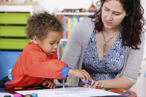 Caregiver watches child squeeze glue on his art project.